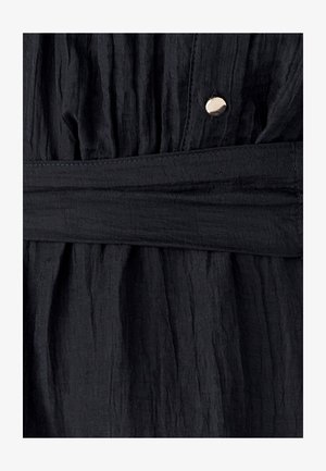 Zwarte textuurstof met een gekreukt uiterlijk heeft een bijpassende riem en een glanzende metalen knoopaccent nabij de taille.