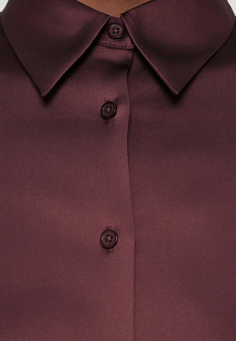 Dunkelrot-satinin Hemd mit spitzem Kragen und drei sichtbaren runden Knöpfen, die vorne geschlossen sind.