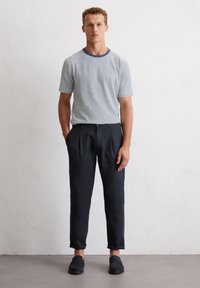 T-shirt rayé gris et blanc avec un col marine, associé à un pantalon gris foncé. Le pantalon a une coupe décontractée et des ourlets retroussés.