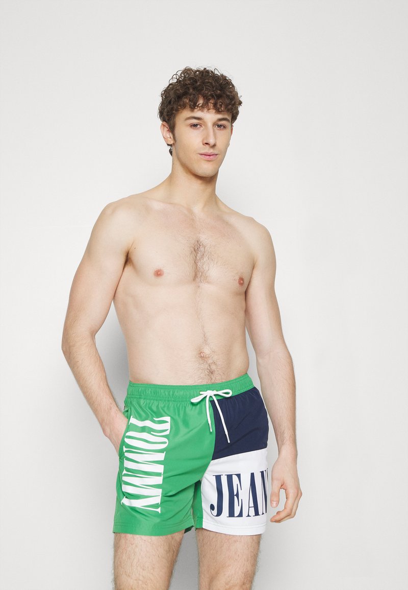 Costumi da bagno verde e blu navy con scritte bianche. Presentano un girovita con lacci e un design a blocchi di colore. Realizzati in materiale leggero.