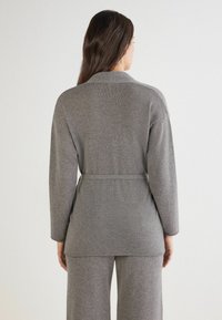 Ropa de punto gris con cinturón, que presenta un cuello chal y mangas largas. Textura suave con detalles de costura visibles a lo largo de los bordes.