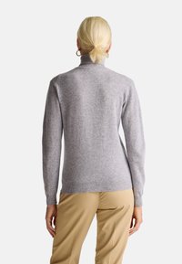 Maglione a collo alto grigio chiaro realizzato in un tessuto morbido, con maniche lunghe e orlo a costine. Abbinato a pantaloni beige.