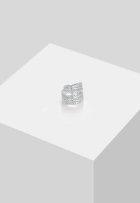 Hõbedane lehekujundusega sõrmus, millel on keerduv disain ja keerukad detailid pinnal, esitatud valgel podiumil.