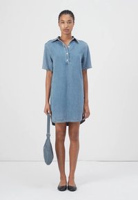 Denim skjortekjole i lys blå, med korte ærmer, en knappet krage og en rett snitt. Kombinert med en grå skulderveske.