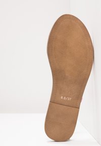 Semelle de chaussure en caoutchouc brun avec surface texturée, comportant des marquages de taille "6,5/37" et un bord lisse et incurvé.