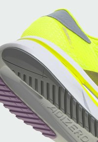 Baskets de course jaunes vives avec un dessus texturé, des accents gris, une semelle intermédiaire blanche et une semelle extérieure rayée de violet avec de profonds crampons.