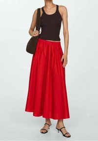 Jupe rouge, longueur cheville avec un design plissé. Portée avec un débardeur noir à côtes et un sac à épaule marron foncé. Sandales noires ajustables.