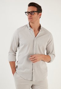 Camisa de algodón de color claro con rayas, que presenta un cuello tipo button-down, mangas largas enrolladas en los puños y un corte regular.