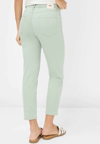 Pantaloni aderenti verde chiaro con vita media, dotati di due tasche posteriori e un'etichetta con il marchio. Tessuto liscio e lunghezza alla caviglia.