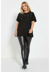 Camiseta negra de manga corta con un diseño brillante en el escote. Combinada con leggings negros brillantes y botines.