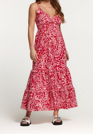 Vrouw die een rood-wit patroonloze mouwloze maxi-jurk draagt met een V-hals en een gelaagde rok, gecombineerd met witte instapsandalen.