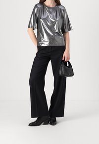 Top corto a maniche corte in metallo argentato, abbinato a pantaloni neri a gamba larga e stivali neri con tacco. Piccola borsa nera come accessorio.