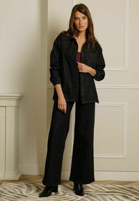 Zwarte denimjas en wijde broekset, met een knoopsluiting, loose fit en een gladde textuur, gecombineerd met zwarte enkellaarsjes.