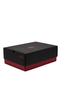 Boîte à chaussures Nike fermée noire et rouge avec logo Nike rouge sur le couvercle, photographiée sur un fond blanc.