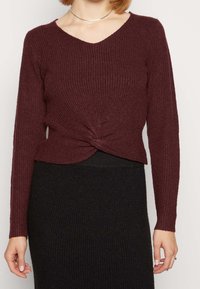 Bordeaux ribben gebreide trui met een V-hals en geknoopte details bij de taille, gecombineerd met een zwarte ribben bodycon rok.