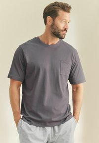 Grå kortärmad t-shirt med rund halsringning och en liten bröstficka. Tyget verkar mjukt, slätt och lätt.