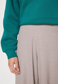 Teal bomulls-tröja med ribbad mudd, ihopparad med ljusbeiga vida, veckade byxor som har en subtil vertikal textur.