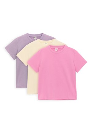 Tre magliette di cotone semplici e a manica corta sovrapposte, colori dal davanti al dietro: rosa, crema e lavanda, esposte su sfondo bianco.