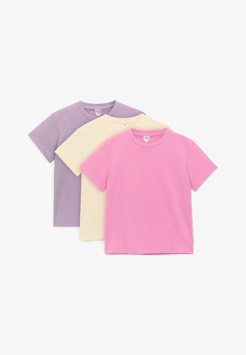 Trois t-shirts en coton unis à manches courtes superposés, couleurs de l’avant vers l’arrière : rose, crème et lavande, présentés sur fond blanc.