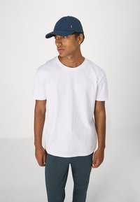 Witte katoenen t-shirt met ronde hals, gecombineerd met een marineblauw pet en donkerblauwe broek. Eenvoudig ontwerp, zachte textuur, geen zichtbare patronen of accenten.