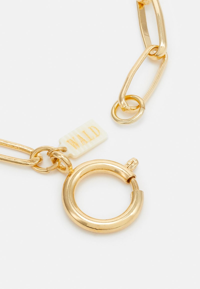 Armband aus goldfarbenem Metall mit ineinandergreifenden Gliedern. Verfügt über einen runden Verschluss und ein weißes Etikett mit der Aufschrift "WALD" in goldener Schrift.