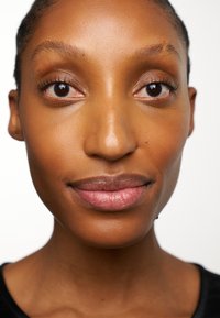 Nahaufnahme eines Gesichts mit glatter, gebräunter Haut, definierten Wangenknochen und natürlichem Make-up, das dunkle Augen und volle Lippen zeigt.