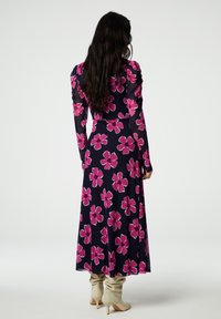 Lang jurkje met een donker marineblauwe achtergrond, versierd met grote roze bloemenpatronen. De stof is glad met gathered mouwen, gecombineerd met beige enkellaarsjes.
