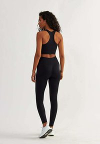 Ensemble sportif noir comprenant un soutien-gorge de sport à dos nageur et un legging taille haute, fabriqué en tissu extensible avec un design ajusté et une texture subtile.