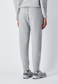 Pantaloni della tuta grigi con una texture morbida, cintura elastica e polsini a coste, abbinati a scarpe sportive grigie con dettagli del logo.