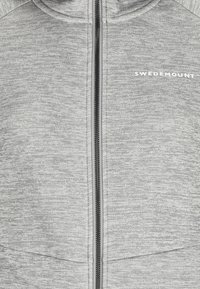 Giacca grigia con zip realizzata in tessuto testurizzato, dotata di cappuccio, zip nera e logo bianco sul lato sinistro.