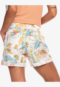 Shorts en tissu blanc avec un motif coloré de feuilles tropicales, dotés d'une taille élastique, de deux poches arrière et d'un ourlet roulé.