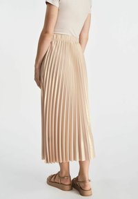 Plisowana spódnica midi w jasnym beżu, z wysokim elastycznym pasem, błyszczącą strukturą i równomiernie rozmieszczonymi fałdami. Połączona z sandałami na cienkich paskach.