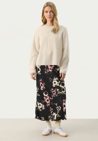 Pull en velours côtelé crème associé à une jupe midi à motifs floraux noirs avec des accents roses et beiges, porté avec des baskets blanches.
