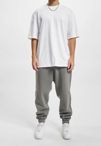 Camiseta blanca de gran tamaño con mangas cortas, combinada con pantalones deportivos grises con puños elásticos. Se lleva con zapatillas blancas.