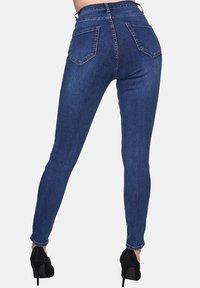 Jeans skinny de cintura alta en denim azul oscuro. Presenta dos bolsillos traseros y costuras contorneadas. Combinados con zapatos de tacón alto negros.