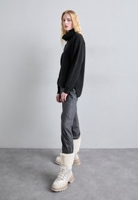 Un pull col roulé noir surdimensionné, un pantalon gris à rayures, et des bottines beiges avec doublure en fourrure. Textures douces et coupe décontractée.