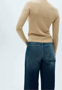 Beige, figurbetontes Sweatshirt mit langen Ärmeln, kombiniert mit hochtaillierten, dunkelblauen Jeans. Das Sweatshirt hat eine weiche Textur; die Jeans haben Gesäßtaschen.