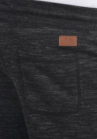 Joggers de tejido texturizado gris oscuro con un bolsillo trasero y una etiqueta de cuero marrón etiquetada como "Solid". Diseño suave y casual, con una cintura elástica.