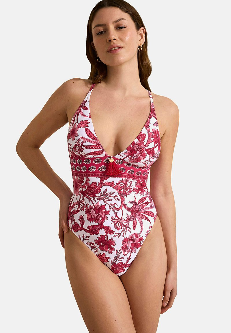 Maillot de bain une pièce blanc avec un motif floral rouge. Décolleté en V profond, bretelles à nouer, ceinture contrastante et détail en franges décoratives.