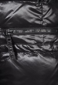 Svart, glänsande material av en puffjacka med en horisontell dragkedjeficka. Slät textur och sömnadsdetaljer är synliga genom hela tyget.