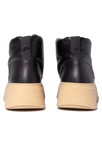 Par de botas negras hasta el tobillo con suelas gruesas beige, vistas desde la parte trasera sobre un fondo blanco.