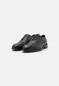 Pantofi din piele neagră, cu un finisaj neted, vârf rotunjit și șase gauri pentru șireturi. Toc ușor ridicat, design minimalist.
