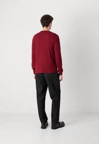 Roestkleurig shirt met lange mouwen, gemaakt van textuurstof, en loszittende zwarte broeken met rechte pijpen en zichtbare naden. Zwarte schoenen.
