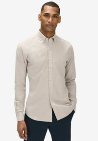 Ljusbeige skjorta med knäppning, spetsig krage, lång ärm och subtil textur. Har en rak nederkant och klassiska knappdetaljer.