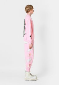 Sudadera rosa con un gran gráfico de mariposa negra en la parte posterior, combinada con joggers rosas a juego que presentan bordados de alas multicolores.