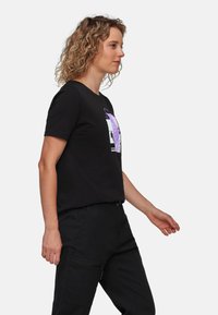 Sort bomulds t-shirt med rund hals og korte ærmer, med et lilla grafisk print på forsiden, parret med sorte cargo-bukser.