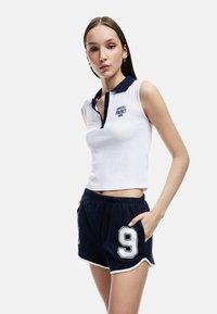 Biała koszulka polo bez rękawów z granatowym kołnierzykiem i haftowanym napisem, w zestawie z granatowymi szortami z białym numerem 9 i bocznymi kieszeniami.