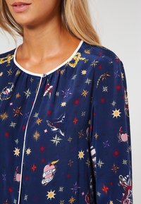 Blusa navy in tessuto morbido con motivi multicolore di stelle e animali, caratterizzata da un collo tondo e chiusura con bottoni a trim bianco.