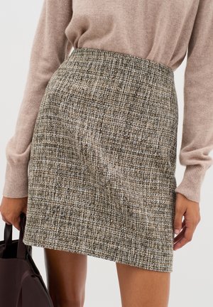 Mini-jupe en tweed avec un motif texturé marron et crème, dotée d'une taille haute. Assortie à un pull beige clair et à un sac foncé.