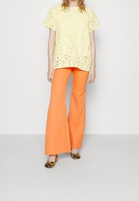 Haut jaune en dentelle à manches courtes, associé à un pantalon évasé orange. Les chaussures présentent un motif serpent et un talon haut.